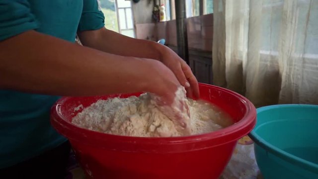 Woman adding water to a dough for bread she is making with bare hands in a red plastic bowl, close up, georgian traditional food