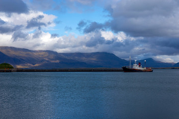 Ship against the backdrop of picturesque mountains and rain clouds entering the bay of the port of Reykjavik, Iceland