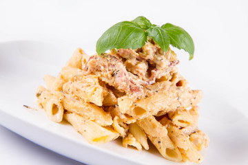 Pasta - penne with white cream sauce with bacon and jalapeño peppers on a plate, decorated with fresh basil	