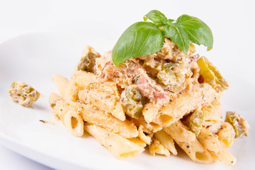 Pasta - penne with white cream sauce with bacon and jalapeño peppers on a plate, decorated with fresh basil	