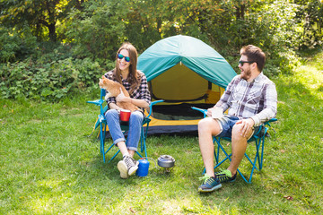 people, summer tourism and nature concept - young couple sitting near a tent