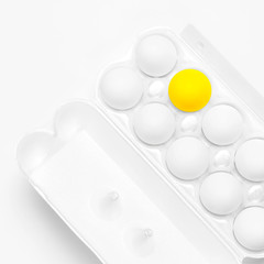 White chicken eggs and one yellow egg in white packaging on light background top view flat lay. Eggs in box, natural healthy food and organic farming concept. Creative minimalistic background, Easter