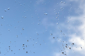 Sky view through window with rain drops on blue blurred backgroud. - Image