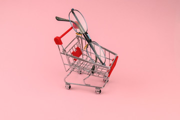 Shopping cart with glasses for sight on pink background. Concept of  glasses purchase, ophthalmology business