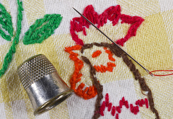 Embroidering with rooster, thimble, needle and thread.