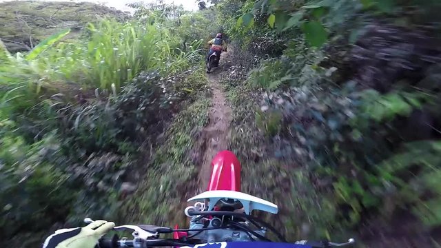 POV of a two riders on a trail in theirs dirt bike, going really fast in a dangerous path in the middle of the nature and florest