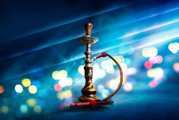 Hookah with smoke on the background of an empty scene, wet asphalt and colored neon light, blurry...