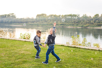 Naklejka premium Children and nature concept - Little Brothers trying to catch soap bubbles