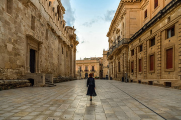Obraz premium Young woman walking across the main street of the island Ortigia in the early morning, Syracuse in Sicily, Italy
