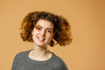 Portrait of beautiful cheerful redhead girl with flying curly hair smiling laughing looking at camera over yellow background.