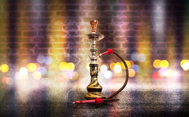 Hookah with smoke on the background of an empty brick wall, wet asphalt and colored neon light, blurry lights of the night city, bokeh