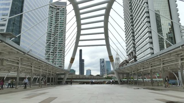 Time lapse video of people travelling under a massive metal structure. with a huge buildings as a background