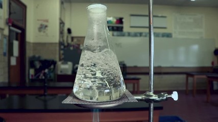 Water boiling in an erlenmeyer flask, heated by bunsen burner in a chemistry classroom - Powered by Adobe