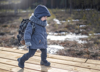 Little boy go hiking with backpack on the forest on a cold day