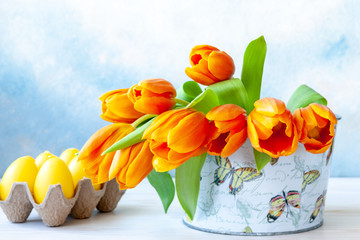 Bouquet of fresh yellow tulip in vase and decorative eggs on sky blue background
