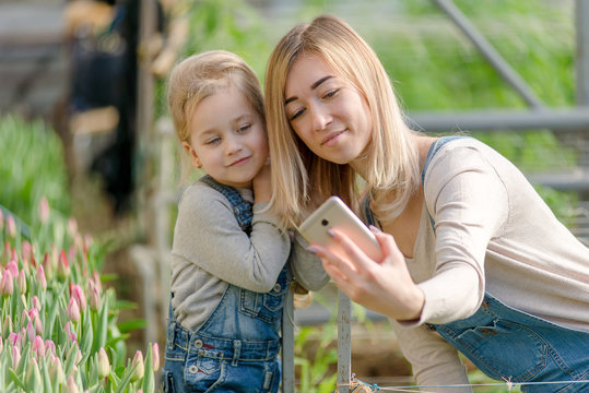 A woman with a small daughter make a selfie in a greenhouse with flowers.