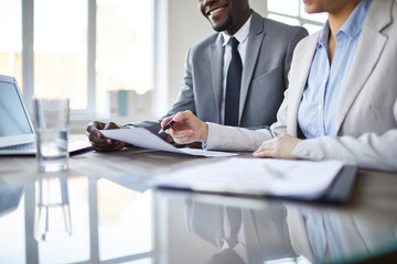 Young elegant woman pointing at paper or contract while negotiating to business partner at meeting