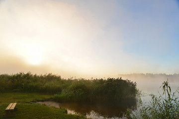 Fototapeta na wymiar Bright light of the rising sun in the fog near the river