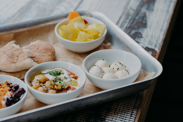 Tasty traditional dish concept. Cropped shot of tray with goat cheese, pita bread, grilled beetroot in bowls on wooden table. Israel food
