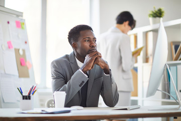 Young pensive or tired broker looking at computer screen while analyzing data or waiting for uploading