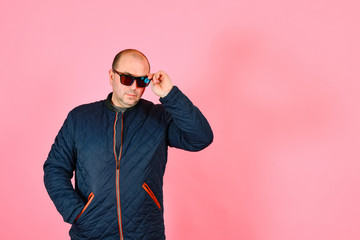 A man in a blue jacket and sunglasses on a pink background in the studio