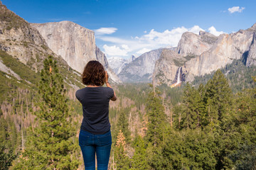Fototapeta na wymiar Young woman is taking a photo of Yosemite valley from Tunnel View in Yosemite National park, United states of America