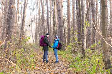 Fototapeta premium adventure, travel, tourism, hike and people concept - smiling couple walking with backpacks over autumn natural background