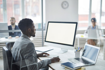 Young confident broker looking at computer screen while searching for online data for his project...