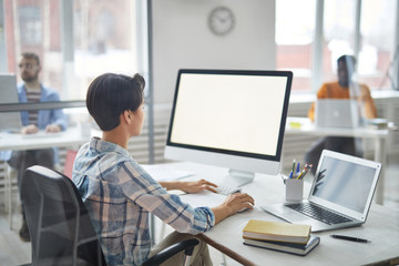 Young busy manager in casualwear sitting by desk in front of computer screen while working with...