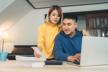 Young asian couple managing finances, reviewing their bank accounts using laptop computer and...