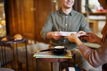 Young colleague passing papers to businesswoman during working meeting by cup of tea in cafe