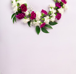 Floral wreath made of white and dark pink or violet carnation cloves flowers with green leaves on light lilac background, top view copy space