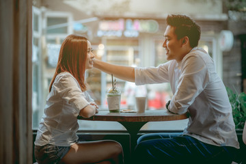 Asian couple talking happily in the cafe during the daytime. - obrazy, fototapety, plakaty