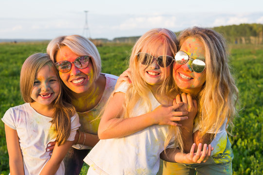 Festival of holi, friendship, happiness and holidays concept - little girls and women in glasses hugging on the festival of Holi.