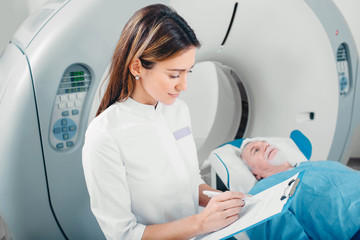 Radiologist write into medical chart after CT Scan in hospital.CT Scan senior patient