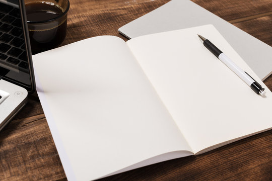 top view image of open notebook with blank pages next to cup of coffee on wooden table. ready for adding text or mockup.