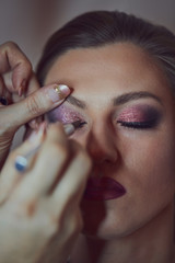 Obraz premium Young beautiful woman applying make-up by make-up artist. Process of making makeup.