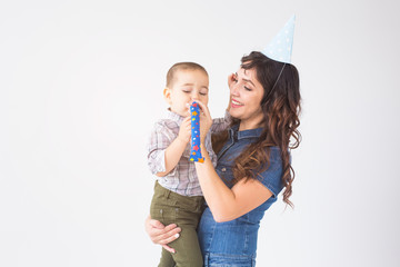 Children, family and holidays concept - young mother in birthday hat holding little son on white background