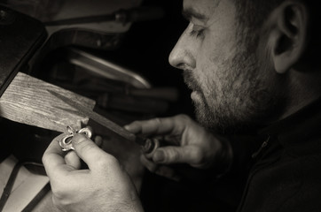 The master jeweler holds the working tool in his hands and makes jewelery at his workplace in the...