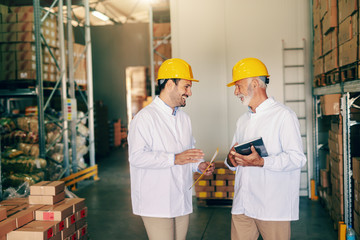 Two workers in white uniforms and protective helmets on heads talking about work. Younger one...