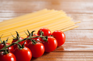 Spaghetti and cherry tomatoes on a wooden table. Homemade food or restaurant. Ingredients for cooking. National Italian healthy food. Close-up.