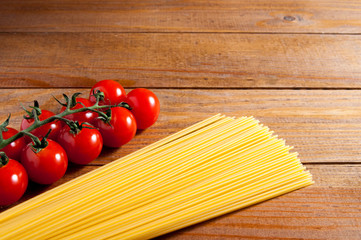 Spaghetti and cherry tomatoes on a wooden table. Tomatoes to the left of spaghetti. Homemade food or restaurant. Ingredients for cooking. National Italian healthy food.