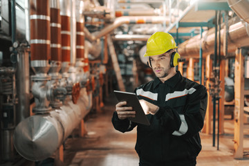 Caucasian worker in heavy industry plant with helmet and in uniform using tablet for work.