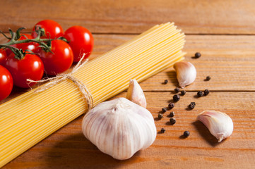 Bunch of raw spaghetti tied with rope, tomatoes cherry, bulb and slices of garlic and pepper on brown wooden background.