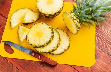 fresh ripe tropical pineapple cut into slices on a yellow rackside lying on a wooden table