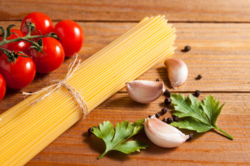 Bunch of raw spaghetti tied with rope, tomatoes cherry, slices of garlic, parsley leaves and pepper on brown wooden background.