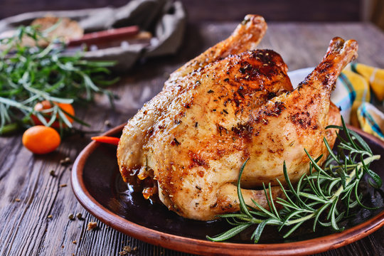 Delicious, freshly baked, crispy, baked chicken is appetizing served on a ceramic dish next to a sprig of fragrant rosemary