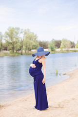 A pregnant girl in a hat walks along the river bank