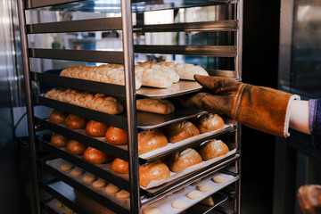 close up view of woman holding holding rack of rolls in a bakery.