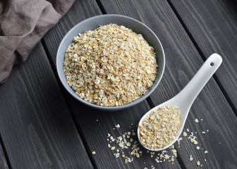 Rolled oats in ceramic bowl and spoon on dark wooden table with texture